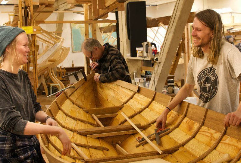 Båtdeltagare på var sin sida om en båt i verkstaden